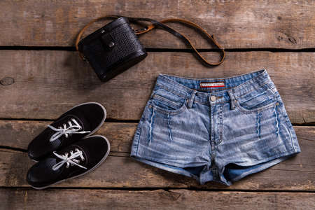 Woman's denim shorts with handbag. Retro clothing on wooden table. Summer sale at vintage boutique. Lady's classic clothes for summer.の写真素材