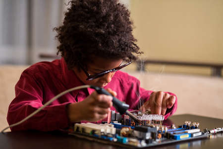 Afro boy soldering motherboard. Darkskinned boy solders motherboard. I know what to do. Very specific hobby.の写真素材