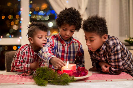 Black boys light Christmas candles. Children lighting red Christmas candles. Christmas eve at home. Happy holidays with brothers.の写真素材