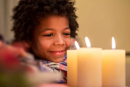 Smiling boy looks at candle. Happy kid beside Christmas candle. New Year shall bring happiness. Feel the holiday atmosphere.の写真素材