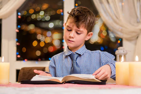 Young kid turns book page. Child reading book at nighttime. Calm holiday atmosphere at home. Bright mind and pure thoughts.の写真素材