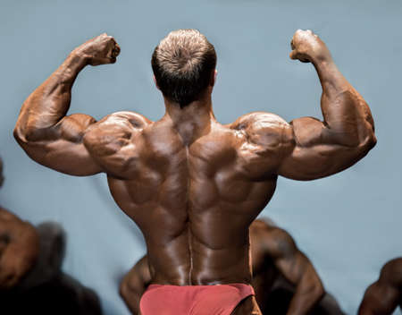 Man's back double biceps pose. Bodybuilder demonstrating arms on stage. Making opponents envious. One more step to victory.の写真素材
