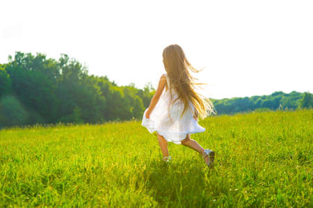 Little girl running on green grass. Beautiful warm summer evening.の写真素材