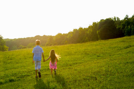 Brother and sister playing in the meadow. Boy and girl holding hands.の写真素材
