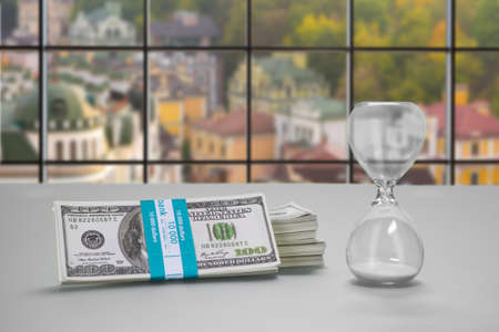 Desk with hourglass and dollars. Bundle of cash and hourglass. Clerk's table at daytime. Real estate...