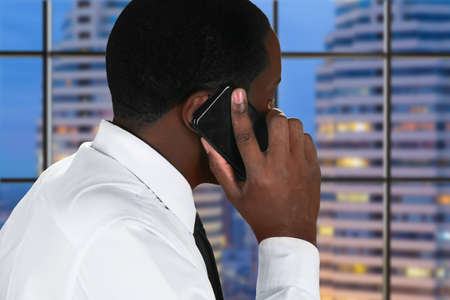 Afro man with mobile phone. Businessman's phonecall on skyscraper background. Evening business...