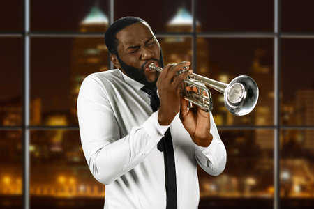 Man in shirt playing trumpet. Black trumpeter in night city. Concert for jazz lovers. Live performance of awesome music.の写真素材