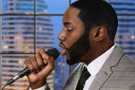 Afro singer with microphone. Singing male on skyscraper background. Recording studio in high building. New single from upcoming album.の写真素材
