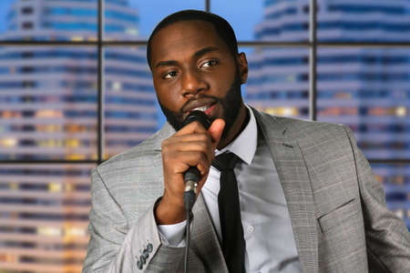 Black man speaks into microphone. Young speaker on evening background. Advice and motivation. Famous expert at business seminar.の写真素材