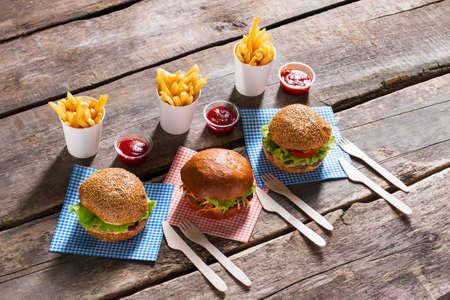 Fries with burgers and cutlery. Old table with burger menu. Crispy fries and juicy hamburgers. Find...