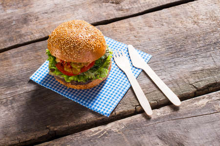 Burger with paper cutlery. Fresh hamburger on old table. Traditional burger with sesame bun. Hearty breakfast in local cafe.の写真素材