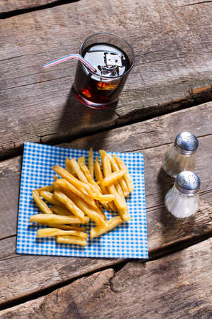Fries on napkin and cola. Cola with fries on table. Crispy snack and sweet drink. Cholesterol and...