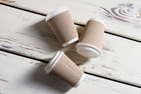 Laying ripple paper cups. Hot drink cups with lids. Disposable cups on white table. Running out of coffee.の写真素材