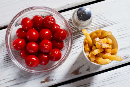 Tomatoes, fries and pepperbox. French fries with red tomatoes. Breakfast snack on white table. Vitamins and energy.の写真素材