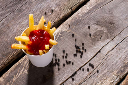 Fries with ketchup and pepper. French fries and whole pepper. Crispy fries on old table. Snack in fast food cafe.の写真素材