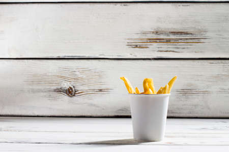 Cup of french fries. White table with fries cup. Crispy and delicious food. High-fat snack in bistro.の写真素材