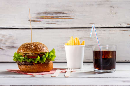 Burger on stick and fries. Cola and fries with burger. White table with beefburger menu. More than enough calories.の写真素材