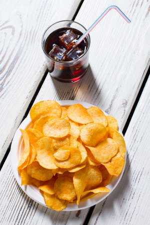 Chips on plate and cola. Glass with drink and chips. Refreshing snack on white table. Classics of fast food.の写真素材