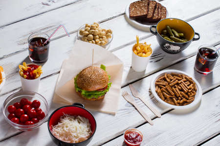 Burger with bread and crackers. Tomatoes, cola and burger. Food on white kitchen table. Sit down and help yourself.の写真素材