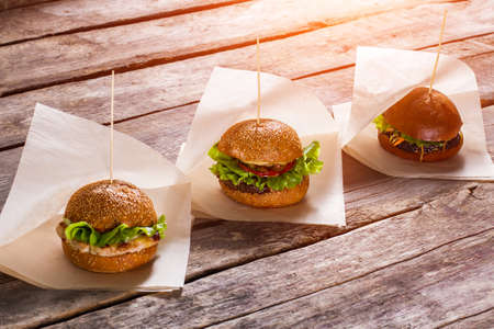 Hamburgers on white wrappers. Old wooden table with burgers. Juicy lettuce and warm buns. Savoury burgers in local bistro.の写真素材