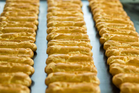 Long rows of eclair shells. Eclairs on wide conveyor belt. Each one has perfect shape. Company's standards of production.の写真素材