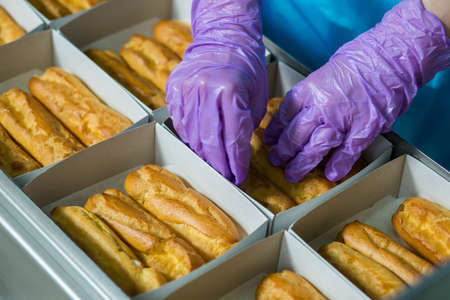Eclairs laying inside white boxes. Hands in gloves touch pastry. Food must be well packaged. Stick to sanitary standards.の写真素材