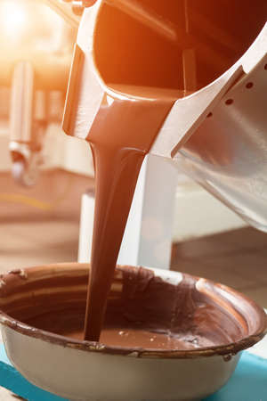 Tank pouring liquid into basin. Brown liquid in metal tank. Production of quality chocolate. Natural melted chocolate.の写真素材