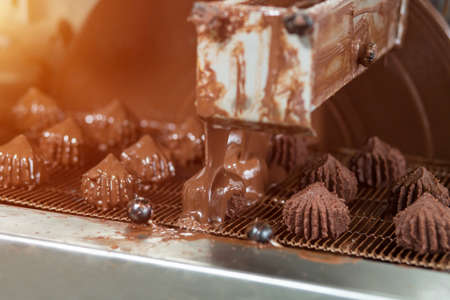 Machine pouring liquid on candies. Conveyor belt with brown sweets. Production of high-quality...
