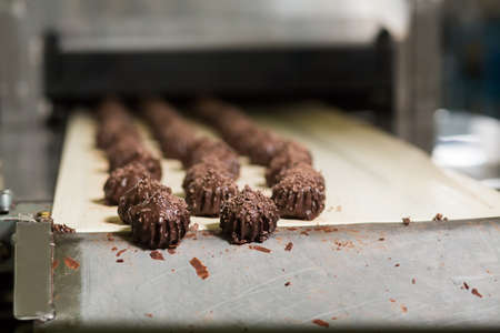 Candies on conveyor edge. Dark brown sweets with shavings. New improved recipe of dessert. Less...