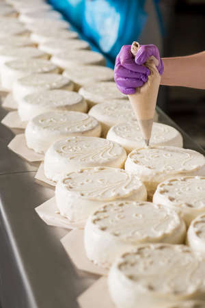 Rows of white cakes. Worker's hand decorating white cakes. Creating a sweet masterpiece. Beautiful handmade ornament.の写真素材