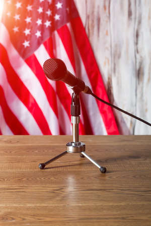 United States flag and microphone. Table with microphone beside flag. Broadcast will soon begin....