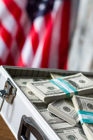 Opened case with dollar bundles. Cash near american flag. Freedom and opportunities. Richness and glory.の写真素材
