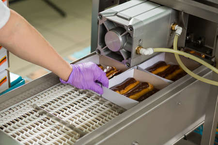 Chocolate eclairs in boxes. Hand touching box on conveyor. Fresh and sweet food. These ones are ready.の写真素材