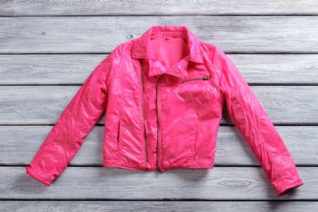 Short pink jacket. Pink jacket on wooden background. Stylish outerwear for girls. Garment made of synthetic fabric.の写真素材