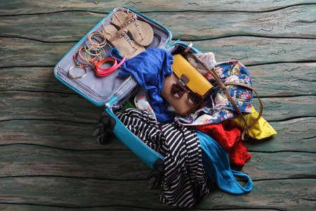 Opened suitcase with crumpled clothes. Sandals and bracelets in luggage bag.の写真素材