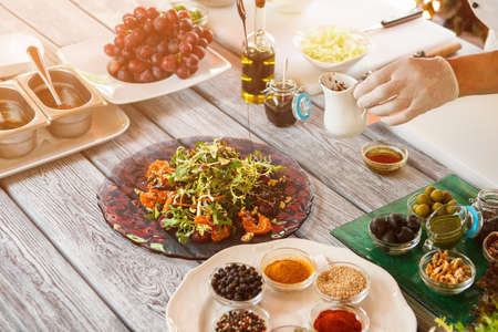 Hand holding small white jug. Salad plate and different spices.の写真素材