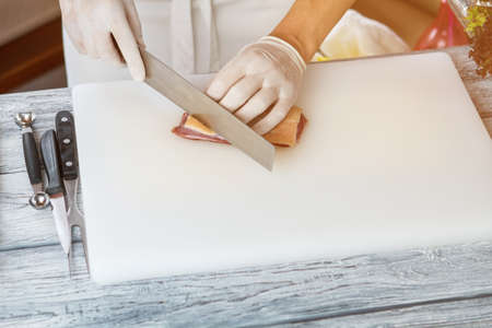 Hand with knife cutting meat on white cooking board.の写真素材