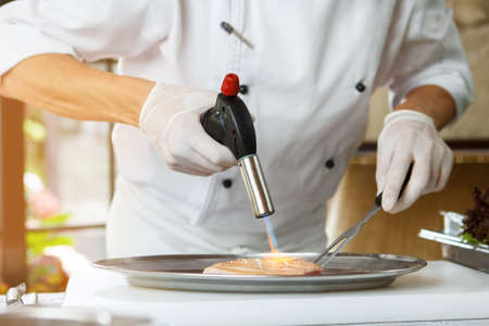 Man's hands hold torch burner. Torch blows fire onto meat.の写真素材
