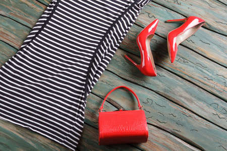 Red glossy heel shoes. Striped dress and a bag. Designer footwear on wooden table. Clothing bought...