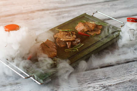 Pieces of meat on tray. Dark tray with cooked meat. Veal medallions with herbs. Food served with dry...