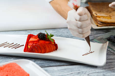 Slices of strawberry on plate. Hand with tool decorates dessert. Liquid chocolate for tasty dessert....
