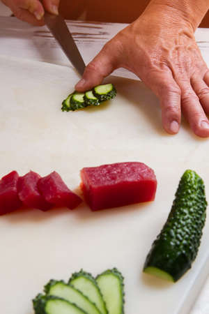 Hand with knife cutting cucumber. Slices of red fish meat. Restaurant chef at work. Vegetable for japanese dish.の写真素材