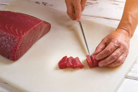 Hand with knife cuts meat. Slices of raw fish meat. Expensive tuna for delicious dish. Chef chose the best fish.の写真素材