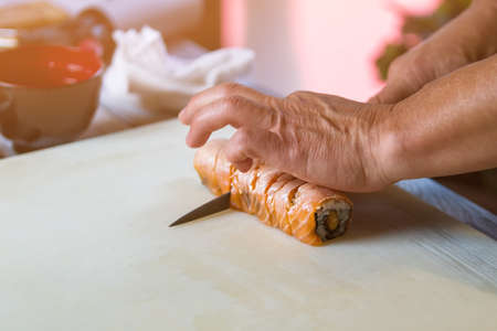 Hands with knife cut sushi. Sushi rolls on cooking board. Traditional uramaki sushi with salmon. New recipe from chef.の写真素材