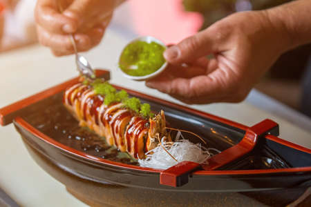 Sushi rolls and white noodles. Spoon puts spice on sushi. Chef adds green caviar. Special ingredient for exquisite dish.の写真素材