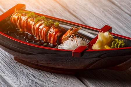 Sushi boat on wooden background. Cooked shrimp beside sushi rolls. Uramaki rolls with soy sauce. Salty sauce and fresh wasabi.の写真素材