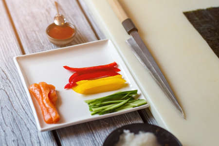 Raw fish and sliced paprika. Knife beside plate with vegetables. Fresh ingredients for sushi rolls. Pieces of ripe bell pepper.の写真素材