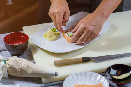 Male hands touch sushi rolls. Sushi and wasabi on plate. New recipe of japanese meal. Uramaki rolls with fish.の写真素材