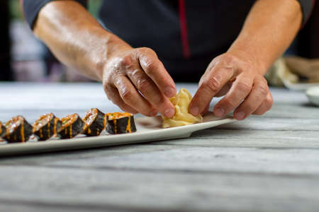 Hands touch sliced ginger. Sushi rolls lying on plate. Traditional hosomaki rolls in restaurant....