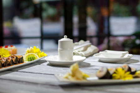 Small white jug beside sushi. Wasabi and sushi rolls. Jug filled with soy sauce. Sit down and help...